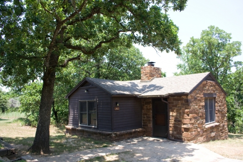 A small stone and wood cabin surrounded by trees on a sunny day.