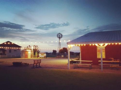 A serene evening scene featuring a red barn, a windmill, and string lights illuminating a gathering area.