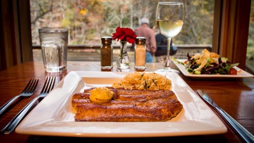 A plate of fish with rice and butter, accompanied by a salad and a glass of white wine, with a scenic view in the background.