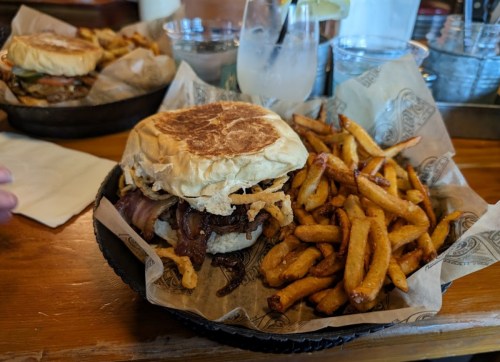 A hearty burger with bacon and crispy onions, served with a side of golden fries in a basket.