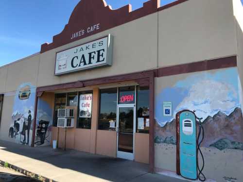 Exterior of Jake's Cafe featuring a colorful mural and an open sign, with a vintage gas pump nearby.