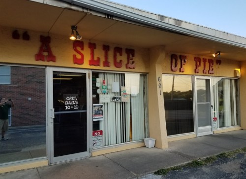 Exterior of a shop with the sign "A Slice of Pie," featuring large red letters and glass doors. Open daily 10-10.