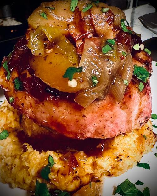 A close-up of a savory dish featuring meat topped with caramelized onions and apples, served on a bed of creamy mash.