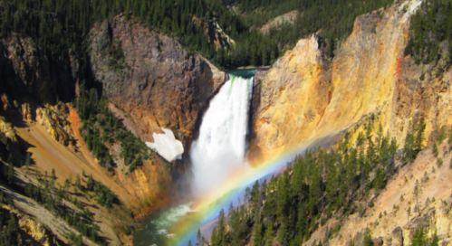 A stunning waterfall cascades down rocky cliffs, creating a rainbow in the mist, surrounded by lush green trees.