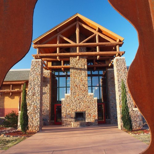 A modern building with a stone facade and wooden accents, framed by a metal sculpture against a clear blue sky.
