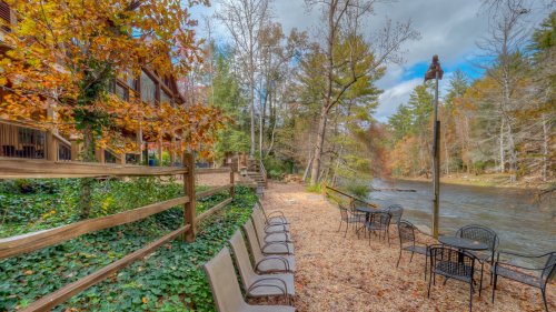 A serene riverside scene with autumn foliage, chairs, and tables along a path beside a calm river.