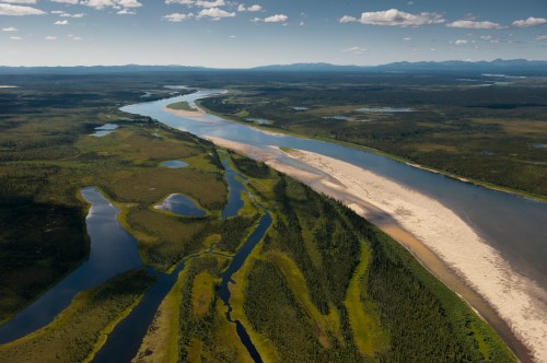 Aerial view of a winding river surrounded by lush greenery and sandy banks under a clear blue sky.
