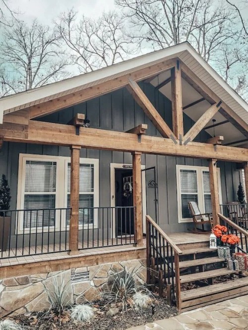 A cozy cabin-style home with wooden beams, a front porch, and seasonal decorations in a wooded setting.