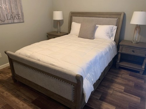 A cozy bedroom featuring a wooden bed with a white comforter, two nightstands, and lamps in a neutral-toned room.