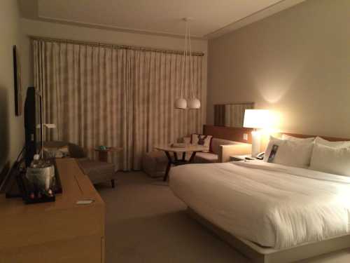 A modern hotel room featuring a large bed, seating area, and soft lighting with curtains drawn.