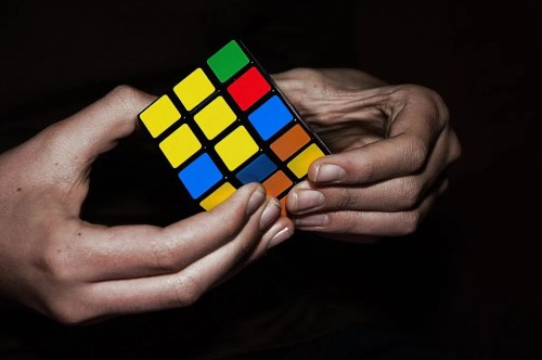A person’s hands holding a partially solved Rubik's Cube with colorful squares.