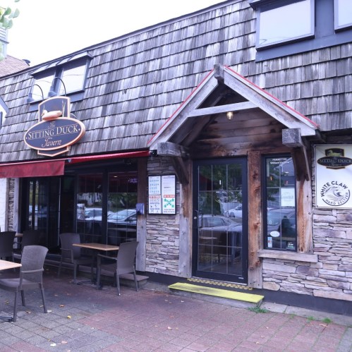 Exterior of Sitting Duck Tavern featuring a wooden facade, sign, and outdoor seating area.