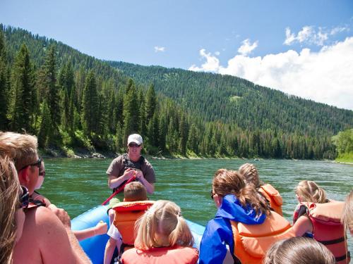 A group of people in life jackets on a raft, listening to a guide on a river surrounded by lush green mountains.