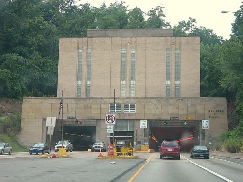 Entrance to the Schuylkill Tunnel, featuring a large, brick building and traffic signals, surrounded by greenery.