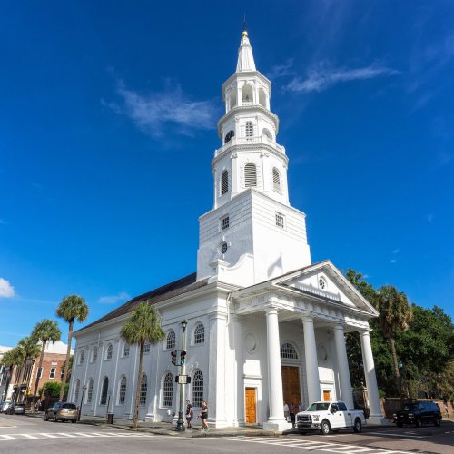 Historic white church with a tall steeple, surrounded by palm trees and a clear blue sky.