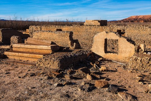 Ruins of an ancient structure with stone walls and steps, set against a clear blue sky and barren landscape.