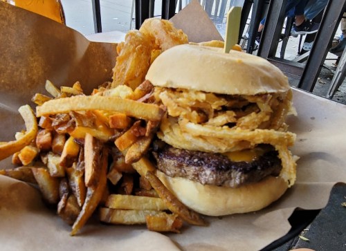 A juicy burger topped with crispy onion rings, served with a side of golden fries on a paper-lined plate.