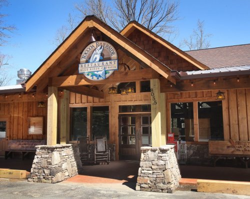Exterior of a rustic wooden restaurant with a stone entrance and a sign reading "Toccoa Riverside Restaurant."