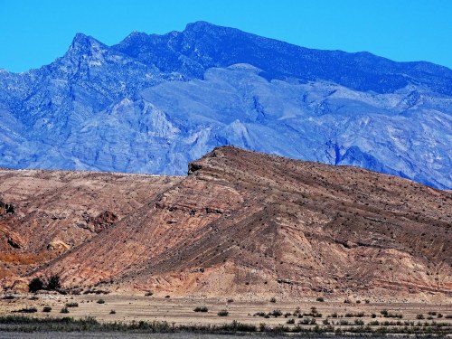 A rugged landscape featuring layered mountains under a clear blue sky, with arid terrain in the foreground.