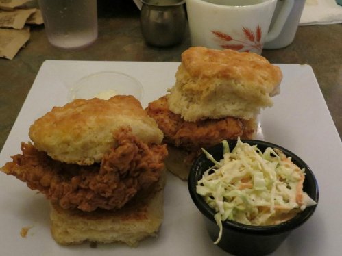 Two fried chicken biscuits served with a side of coleslaw and a small cup of butter.