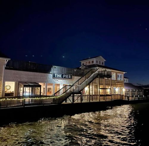 A waterfront building named "The Pier" illuminated at night, with a staircase and reflections on the water.