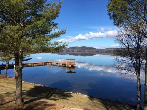 A serene lake scene with a wooden dock, surrounded by trees and mountains, reflecting a clear blue sky.