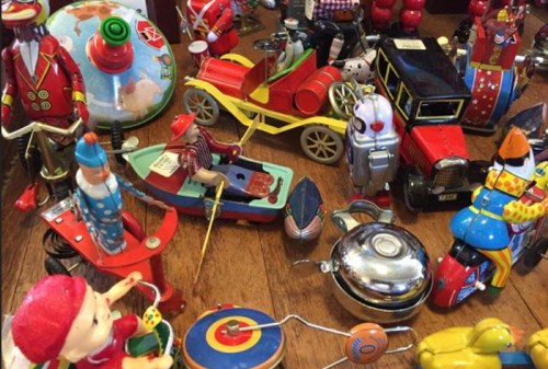A colorful assortment of vintage toy cars, figures, and mechanical toys arranged on a wooden surface.