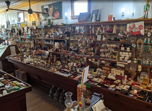 A cluttered antique shop filled with various collectibles, jewelry, and vintage items displayed on wooden shelves.