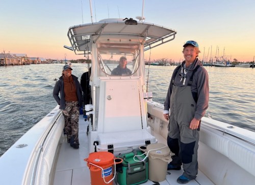 Three people on a boat at sunset, with fishing gear and containers visible in the background.