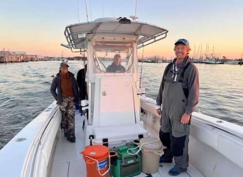 Three people on a boat at sunset, with fishing gear and containers visible in the background.