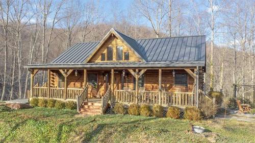 A charming log cabin with a metal roof, surrounded by trees and greenery, featuring a welcoming porch and steps.