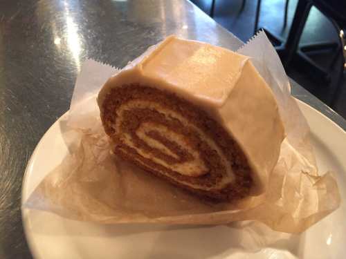 A slice of rolled cake with a creamy filling, wrapped in parchment paper on a white plate.