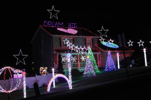 A house decorated with colorful Christmas lights, featuring stars, trees, and the phrase "DREAM BIG" illuminated on the roof.