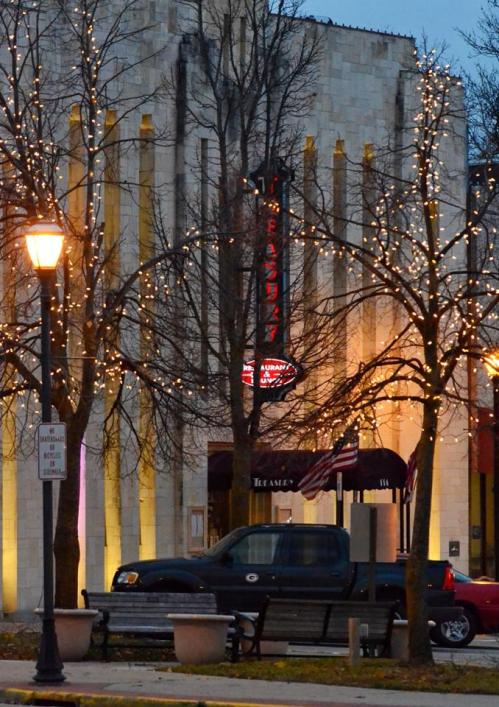 A street view of a building with decorative lights on trees, a parked truck, and a lamppost in the foreground.