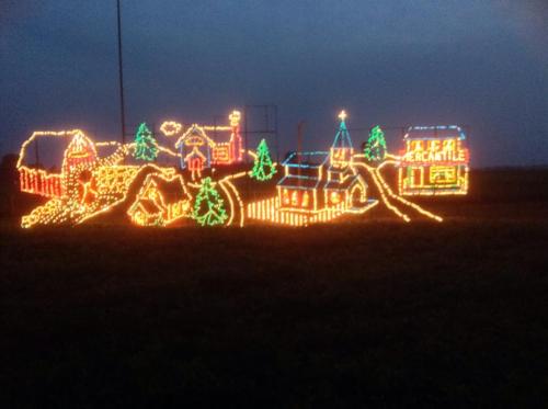 A colorful display of Christmas lights depicting a village scene with houses, trees, and a church against a dark sky.