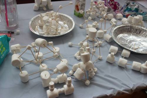 A tabletop covered with various structures made of marshmallows and toothpicks, arranged in clusters.