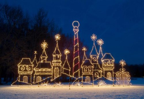 A whimsical display of illuminated holiday buildings and trees against a dark blue sky, creating a festive atmosphere.