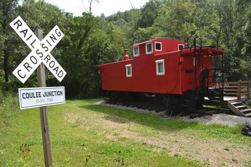 A bright red caboose parked near a railroad crossing sign in a wooded area.