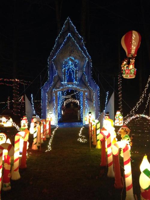 A festive pathway lined with candy cane lights leads to a brightly lit, icy archway decorated for the holidays.