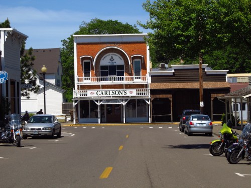 A street view of a historic building labeled "Carlson's," surrounded by trees and parked motorcycles.