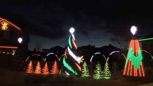 Colorful Christmas lights illuminate trees and decorations against a dark evening sky.