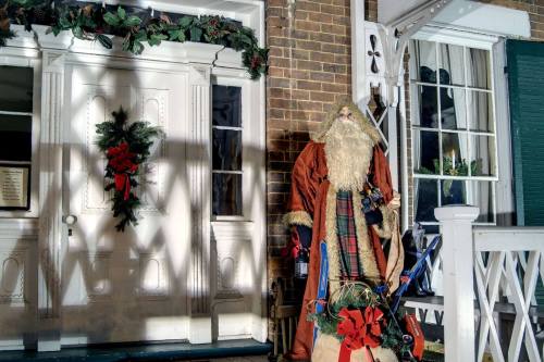 A festive scene featuring a decorated door with a wreath and a Santa figure standing beside it, casting a shadow.