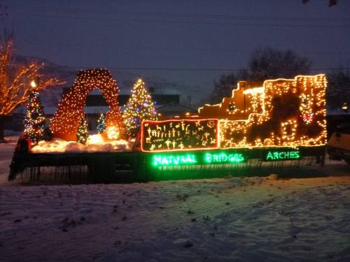 A festive display featuring illuminated arches and trees, with "Natural Bridges Arches" lit up in green, set in snow.