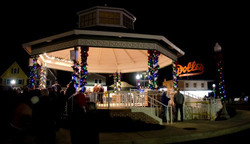 A festive gazebo decorated with lights, surrounded by people enjoying a nighttime event.