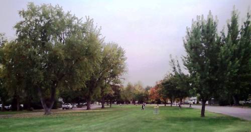 A park scene with green trees, a grassy area, and people walking in the distance under a cloudy sky.