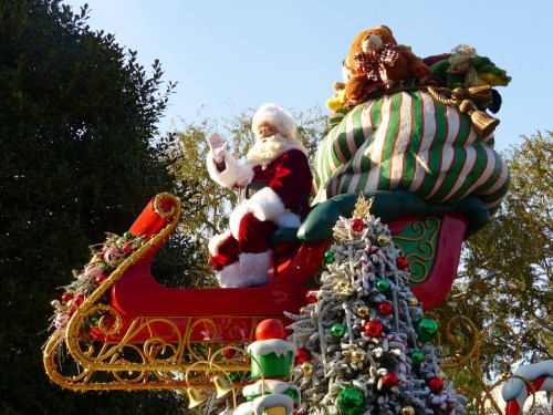 Santa Claus waves from a festive sleigh, surrounded by holiday decorations and a decorated Christmas tree.