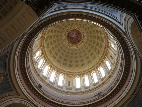 A view looking up at a beautifully decorated dome with intricate patterns and windows letting in natural light.