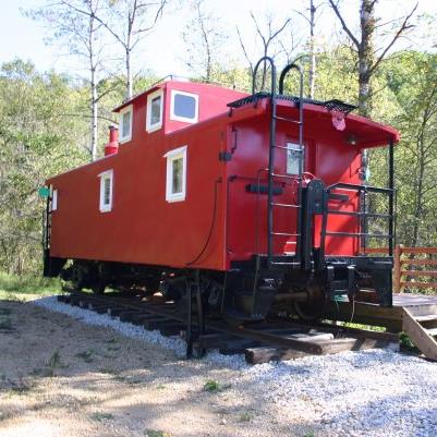 A bright red caboose on a gravel track, surrounded by trees and greenery.