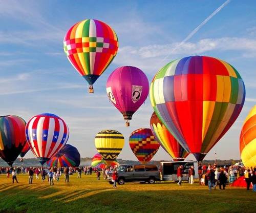 A vibrant scene of colorful hot air balloons in the sky above a crowd at a festival on a sunny day.