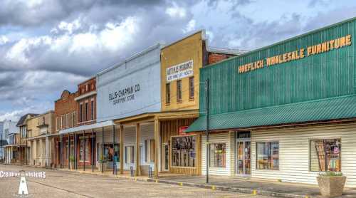 Historic storefronts line a quiet street under a cloudy sky, showcasing vintage architecture and signage.